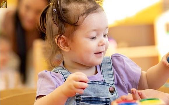 A smiling girl plays at a table in the classroom
