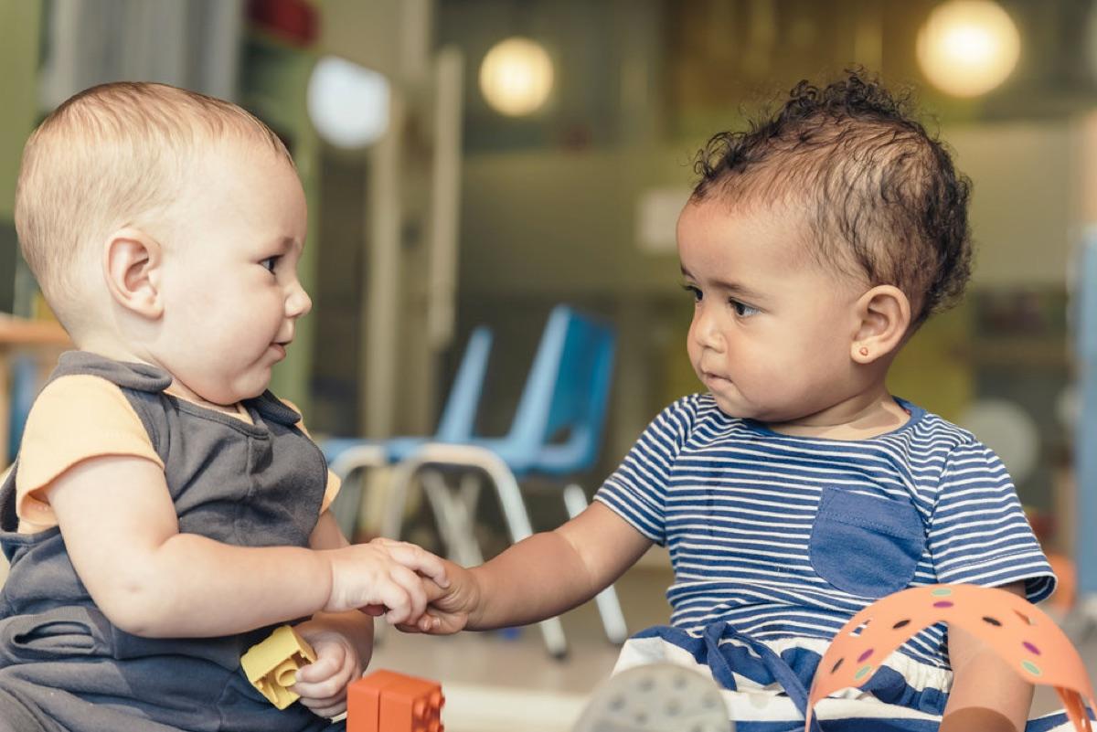 Two babies hold hands while playing with building blocks