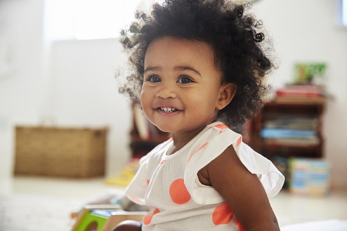 A smiling toddler plays with toys in a bright playroom